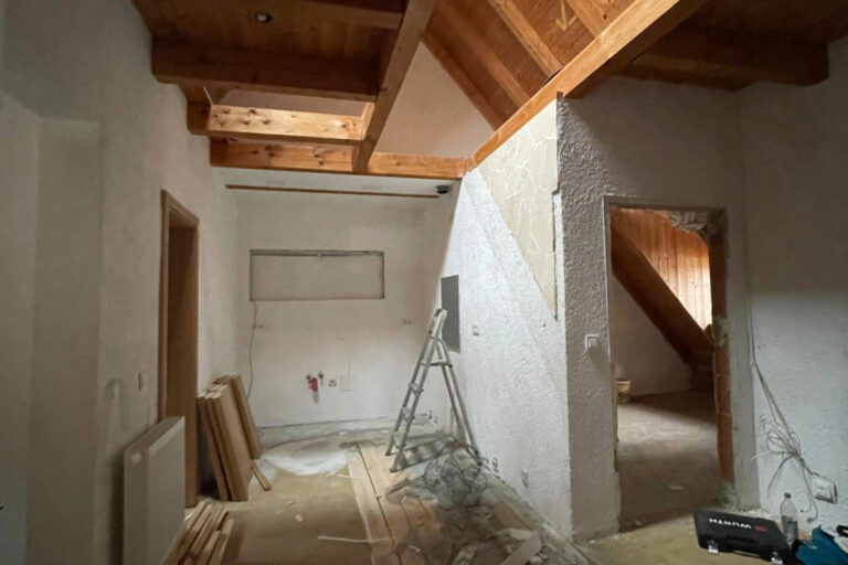 Sleek, well-lit room with white plastered walls and a smooth, polished floor. Electrical cables are neatly tucked into the walls, and a collection of power tools rests atop a ladder placed next to an electric meter box in the corner. Black steel pipes hang gracefully from the ceiling, adding an industrial touch to the space. --ar 31:21